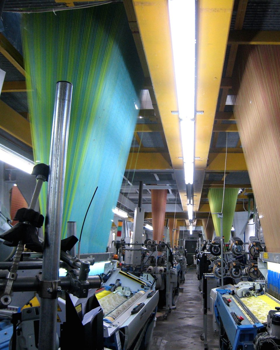 Rows of looms weaving colorful yarn in one of Orr Textile's partner mills